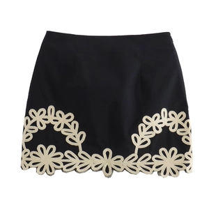 Détail d'une mini-jupe noire avec broderie blanche complexe sur l'ourlet du bas