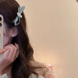 Elegant light blue satin bow hair clip with white pearls worn by a model in a warm setting