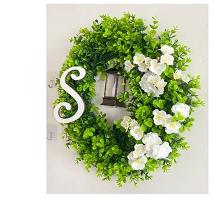 Close-up of Christmas wreath with green leaves, white flowers, letter S, and black lantern