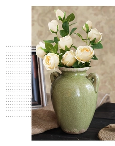 Detail van groene keramische vaas met craquelé glazuur, bloemen en een rustieke afwerking