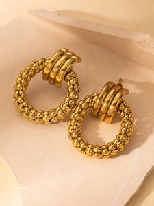 Macro detail of gold-plated hoop earrings with textured weave and smooth metallic finish