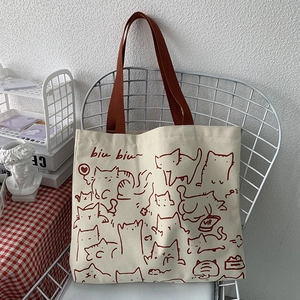 Artistic canvas tote bag with red cat illustration hanging on a metal grid chair