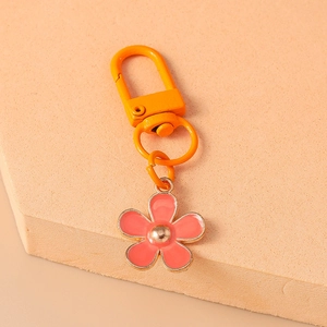 Close-up of a pink flower pendant with an orange metal keychain on a beige background