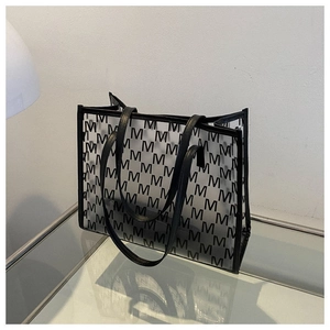 Detail of transparent tote bag featuring black M-letter print and faux leather handles