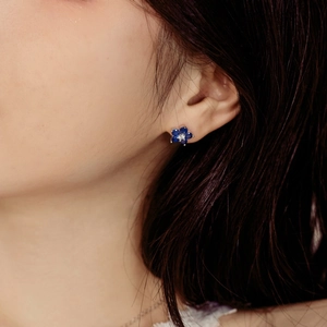 Close-up of elegant flower stud earrings featuring deep blue petals on model's ear