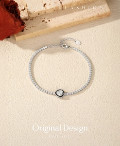 Macro shot of S925 silver tennis bracelet with black heart pendant on a warm background