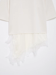 Detail of cream white knit top featuring intricate eyelash lace trim and asymmetric hemline