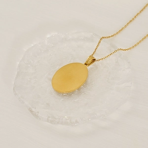 Macro shot of gold stainless steel Virgin Mary oval pendant necklace on white fabric