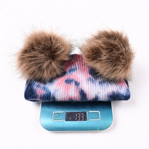Bonnet en maille tie-dye avec deux pompons, affichant 133g sur une balance