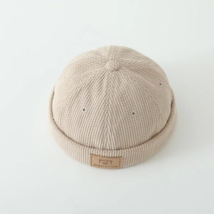 Detailed view of beige corduroy kids beanie with a brown leather cartoon bear patch