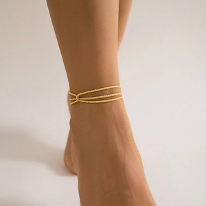 Close-up of triple-layered golden metal anklet shown worn on a woman's ankle