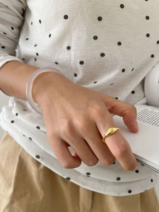 Close-up of a wavy gold-plated ring and translucent purple bangle worn on a hand