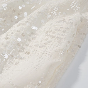 Dettaglio di paillettes scintillanti e trama di rete fine su tessuto crema