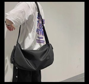 Black nylon messenger bag featuring adjustable strap and woven logo detail on side