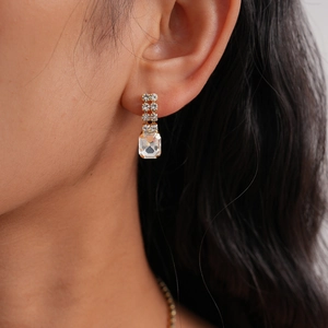 Detailed close-up of emerald-cut crystal earrings with gold plating on female model