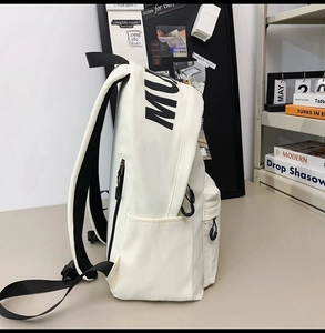 Side view of white canvas backpack showing storage pockets and adjustable black straps