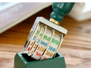 Macro detail of a vintage roller date stamp with a green wooden handle on a desk