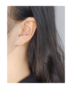 Close-up of heart-shaped pretzel silver stud earrings worn on a woman's earlobe
