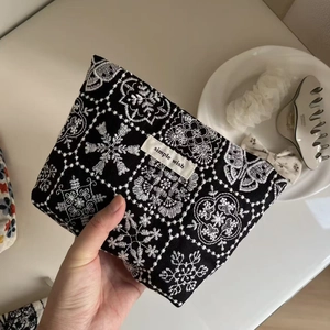 Close-up of black canvas makeup bag with white flower embroidery and Simple Wish label