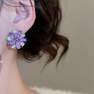 Detailed view of elegant purple flower stud earrings with crystals worn on a female ear