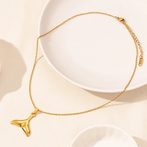 Detailed macro view of a gold whale tail pendant with lobster clasp on a ceramic dish