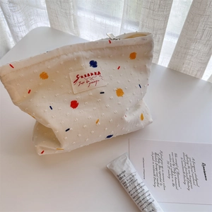 White canvas cosmetic bag with colorful embroidered dots on a bright minimalist desk
