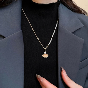 Detail of elegant gold ginkgo leaf pearl necklace worn on a black turtleneck and grey suit