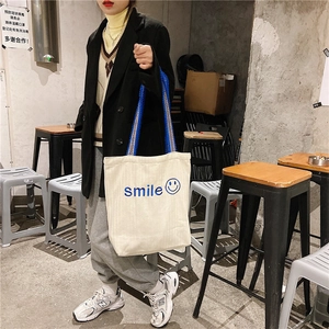 Detail of beige canvas tote with blue smile embroidery and contrast webbed handles