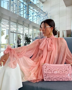 Detail of pink pussy-bow chiffon shirt with ruffled cuffs and lace texture handbag