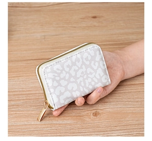 Close-up of a compact leopard print card holder with golden zipper on a wood background