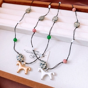 Vue macro de colliers pendentifs cheval avec perles de pierre naturelle sur plateau beige