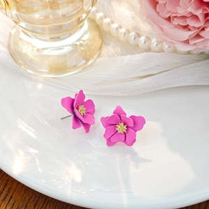 Macro view of magenta floral earrings with yellow stamen on white ceramic plate