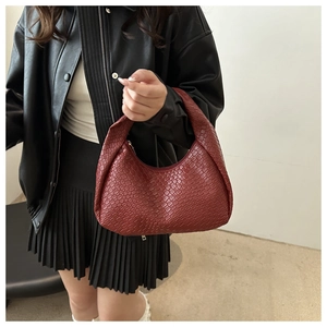 Dettaglio della borsa hobo intrecciata bordeaux tenuta da una modella in giacca di pelle