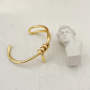 Detail of a twisted knot gold brass cuff bracelet next to a white plaster statue decor