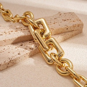 Chunky gold chain necklace with mixed link design on elegant beige travertine background