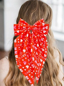 Detail view of a large red bow hair clip with LOVE heart prints worn on a ponytail