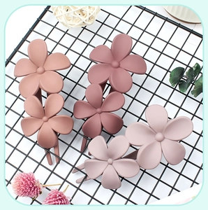 Detail of three matte floral hair clips in pink tones on a black minimalist metal rack