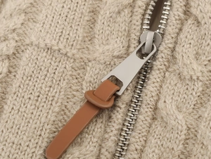 Macro view of beige cable knit sweater featuring a silver metal zipper with brown leather puller