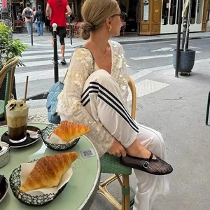 Chic women's white sequin long sleeve blouse and side-striped trousers at a French cafe