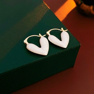 Gros plan de boucles d'oreilles cœur plaquées or avec émail blanc sur écrin