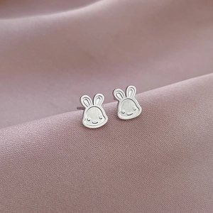 Macro view of silver rabbit stud earrings on soft pink silk background with metallic luster