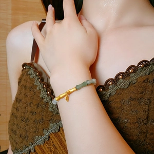 Detailed view of bamboo leaf gold bracelet with green jade beads on a woman's wrist