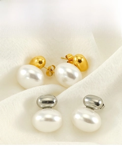 Macro shot of heart-shaped gold and silver pearl earrings on white fabric background