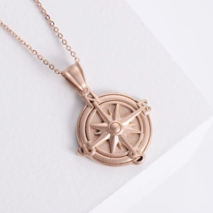 Rose gold stainless steel compass pendant necklace with engraved letters on stone background