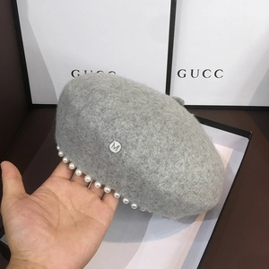 Close-up of a grey wool beret featuring pearl rim decoration and a silver M metal logo