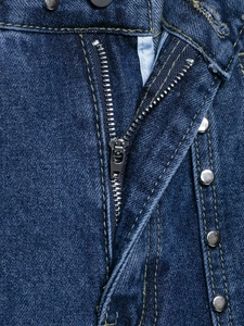 Détails de la braguette zippée en métal et des rivets sur un jean large en denim bleu