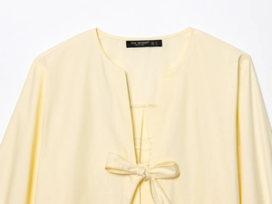 Close-up of light yellow poplin shirt featuring a V-neckline with a delicate bow tie detail