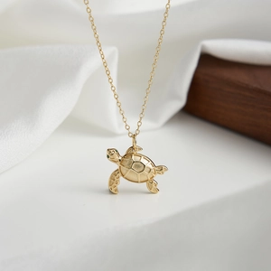 Detail of a gold sea turtle pendant with green crystal eyes on a simple chain necklace