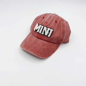 Detail of washed red baseball cap with white MINI towel embroidery on cotton fabric