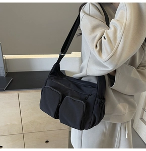 Detail of black nylon crossbody bag featuring dual front zipper pockets and adjustable strap